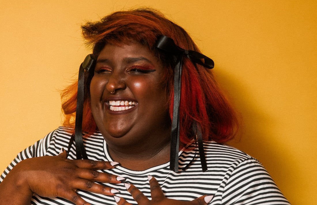 Portrait of sunstoney smiling against a yellow backdrop. Photo credit: Julianna Photography